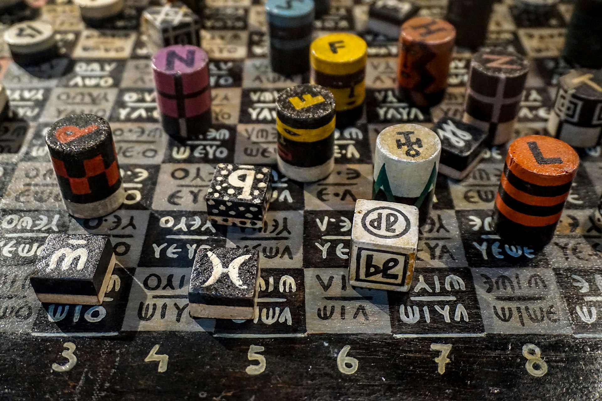An overhead shot of unusual square and cylindrical chess pieces covered in patterns and symbols