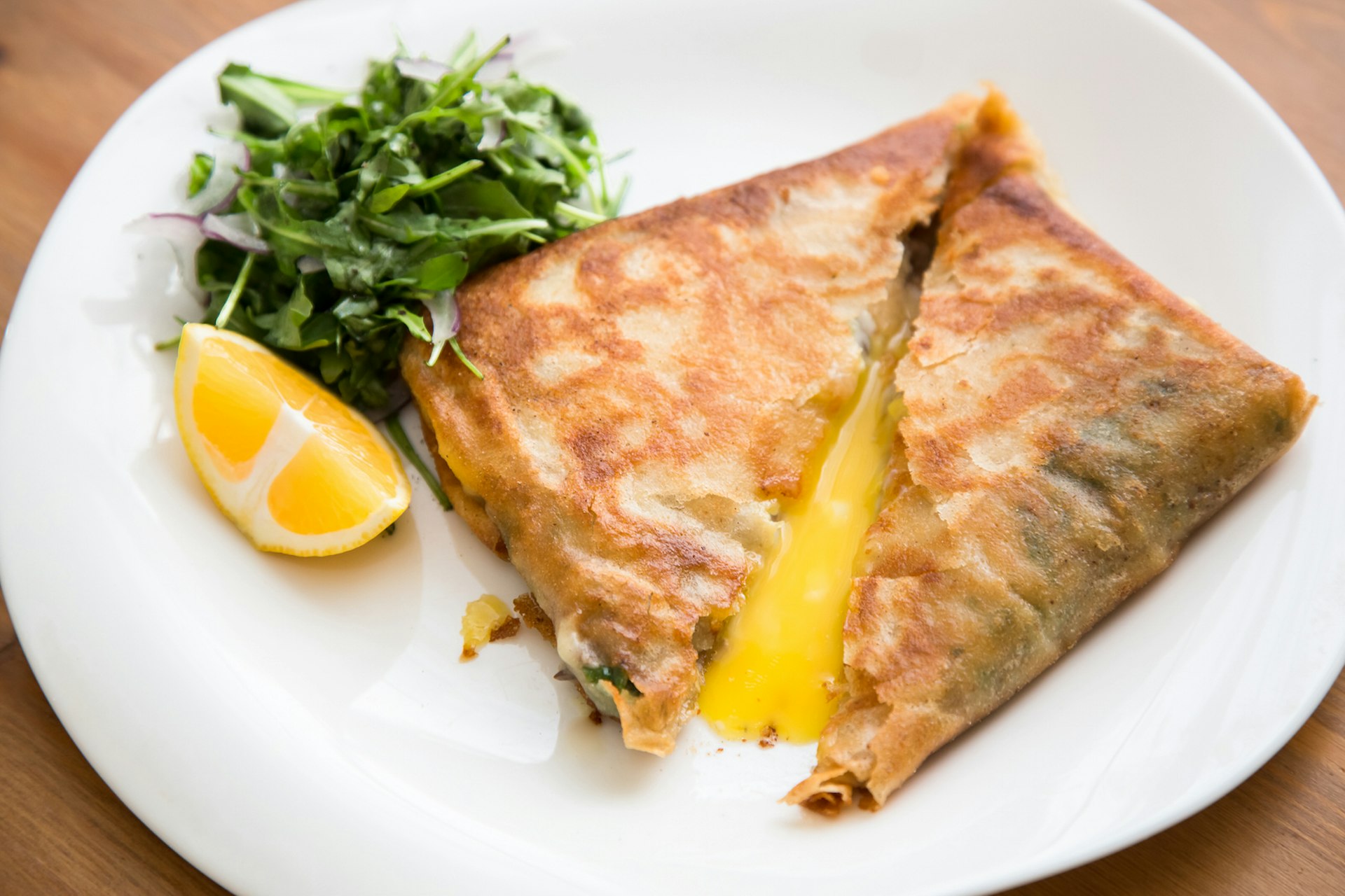 Brik, a classic Tunisian dish made with fried pastry and egg. is on a white plate and garnished with a lemon wedge and a pile of green parsley