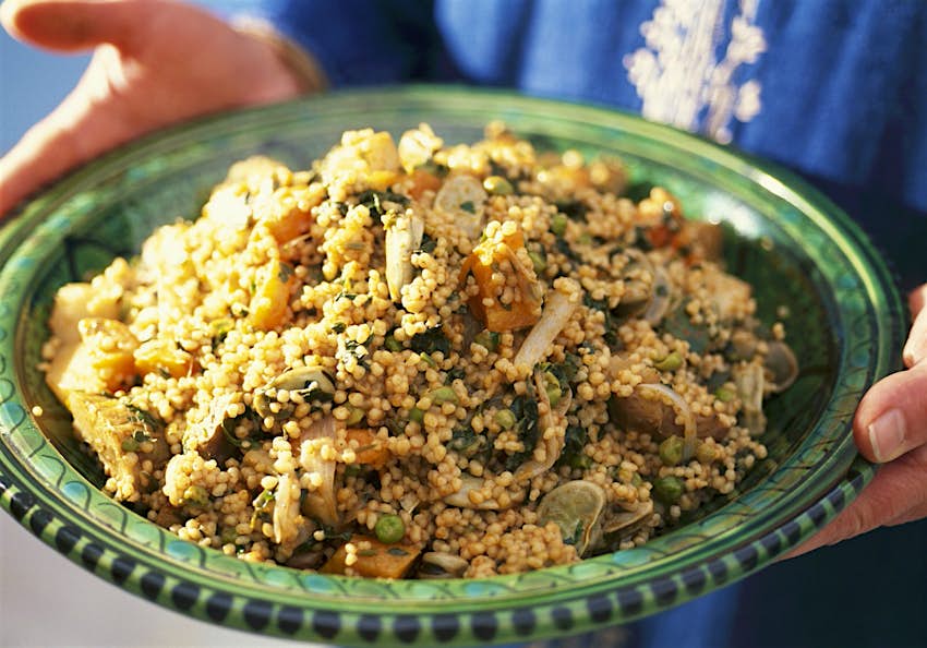 Person holding a green dish of vegetable couscous