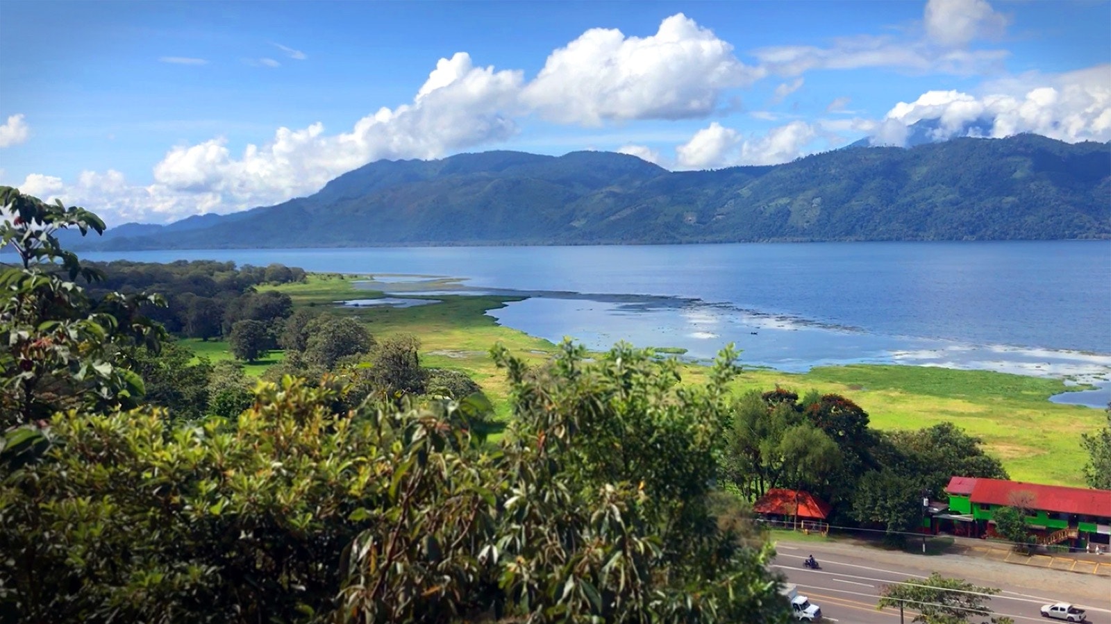 Cars travel along Highway CA-5 in front of Lake Yojoa as clouds move over a collection of mountains in the background © Erik R. Trinidad / Lonely Planet