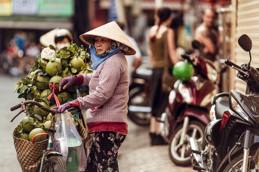 En vietnamesisk kvinna i en konisk hatt säljer färska gröna kokosnötter på gatan i Ho Chi Minh-staden i Vietnam,