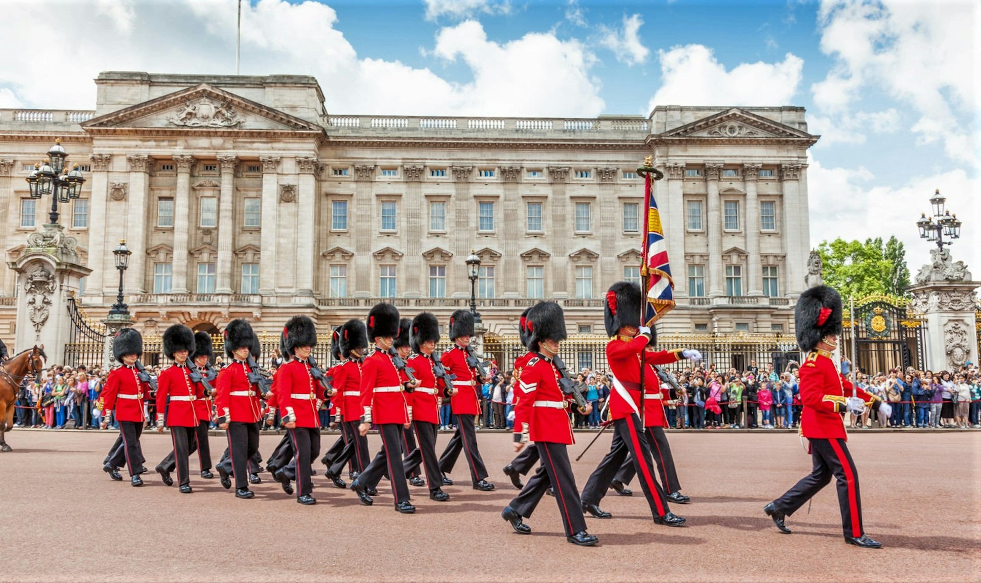 The facade of Buckingham Palace with soldiers marching past.