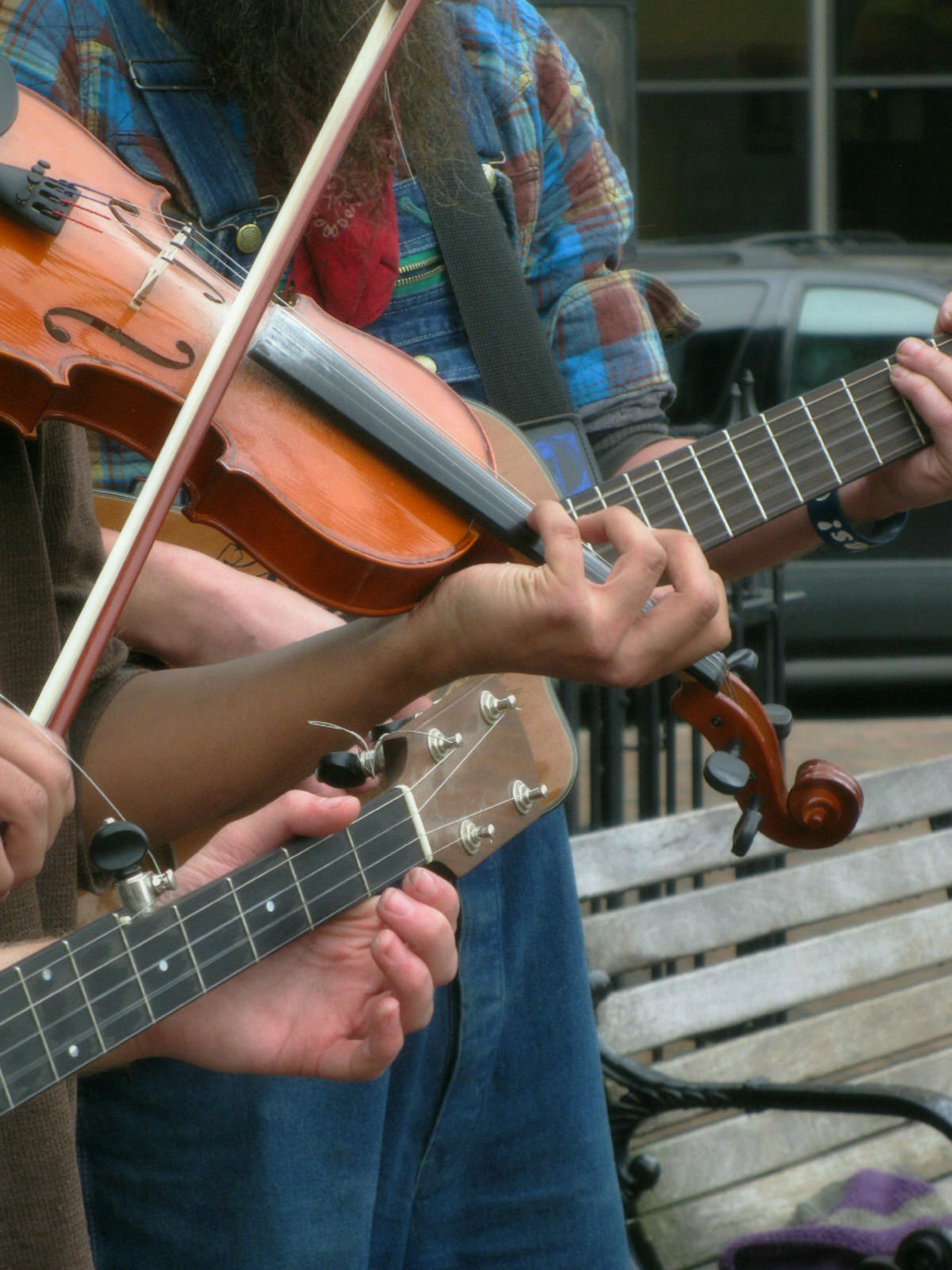 A close-up of a violin and two banjos, and the hands dancing across them, in a typical street scene in Asheville, North Carolina, where busking is part of the thriving music scene..