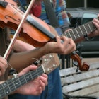 A close-up of a violin and two banjos, and the hands dancing across them, in a typical street scene in Asheville, North Carolina, where busking is part of the thriving music scene..