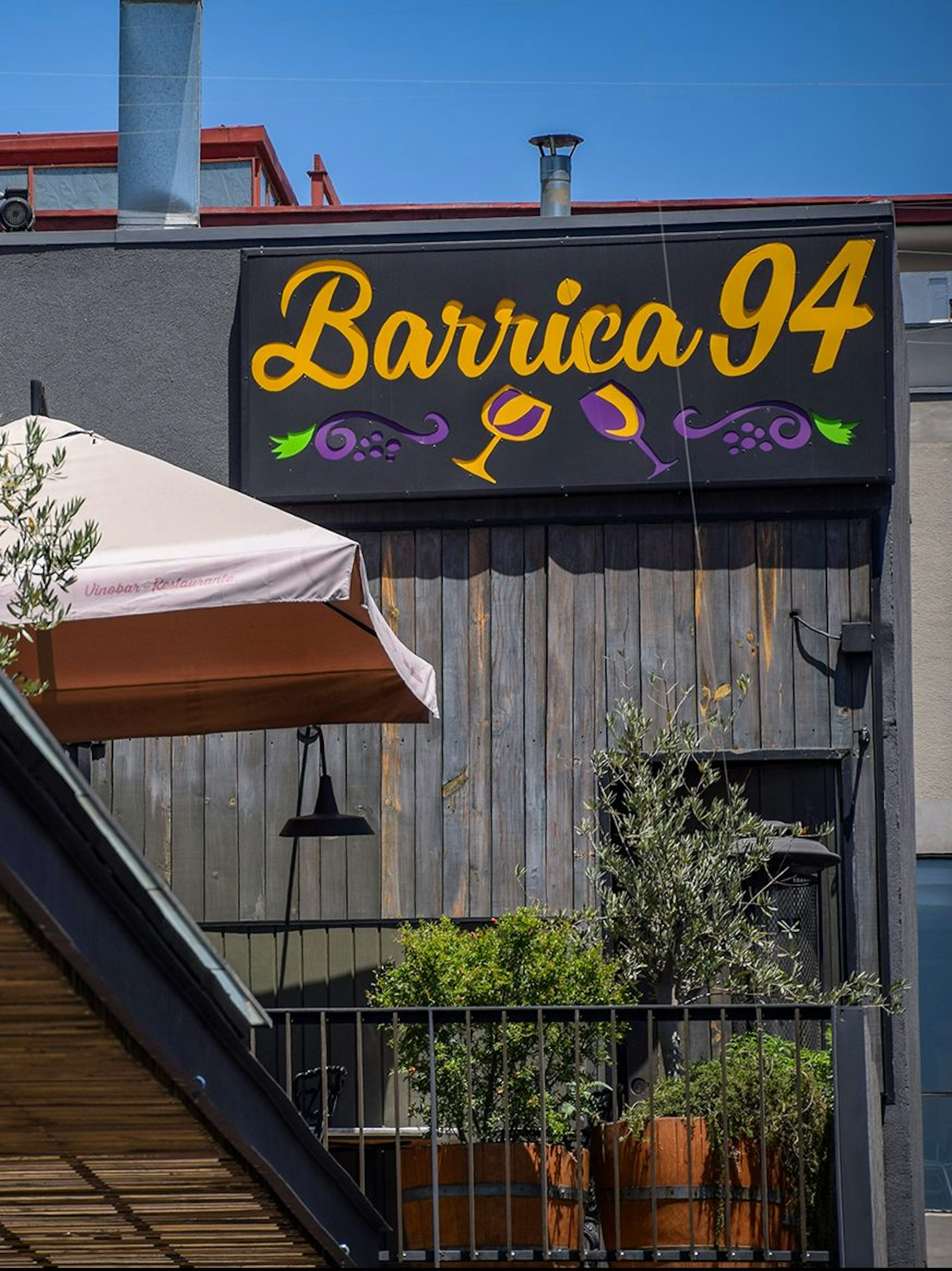 An external shot of the Barrica 94 sign, which features yellow cursive text, purple grapes, and two wine glasses