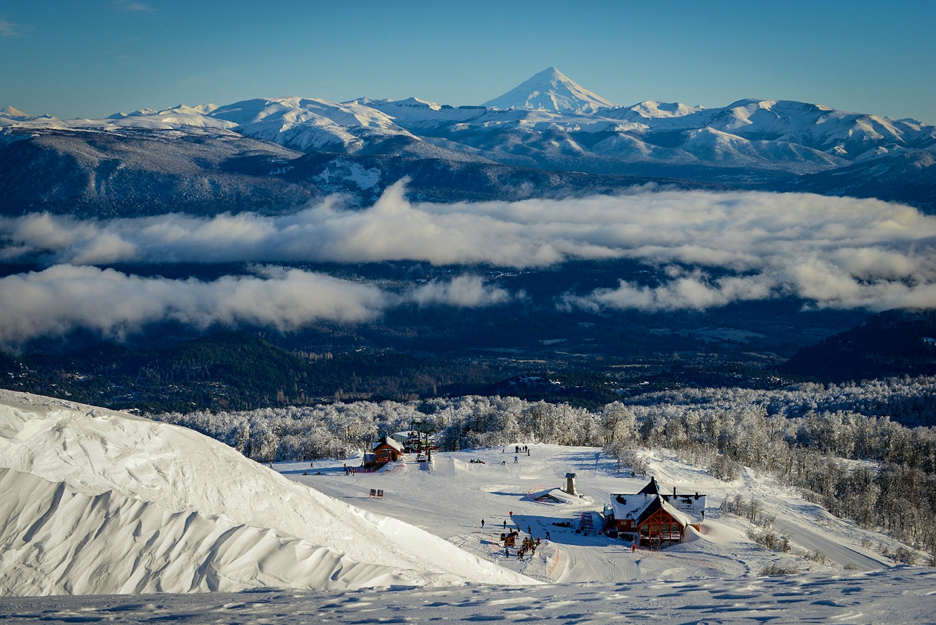 A view of a rocky mountain range from the top of a snowy hill overlooking a ski lodge in Chapelco