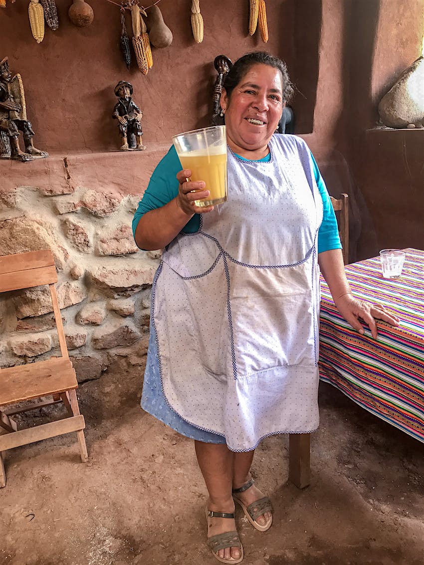 A woman in a white apron smiles at the camera, holding a large glass of beer