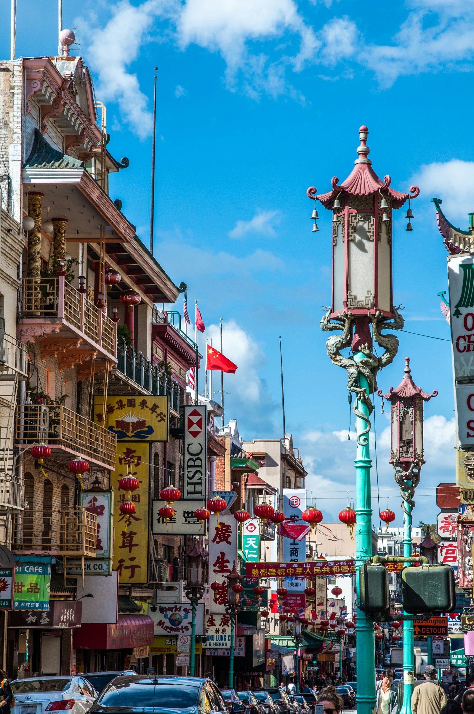 A busy street in San Francisco's Chinatown, red lanterns hang over the street while dragons adorn a streetlight