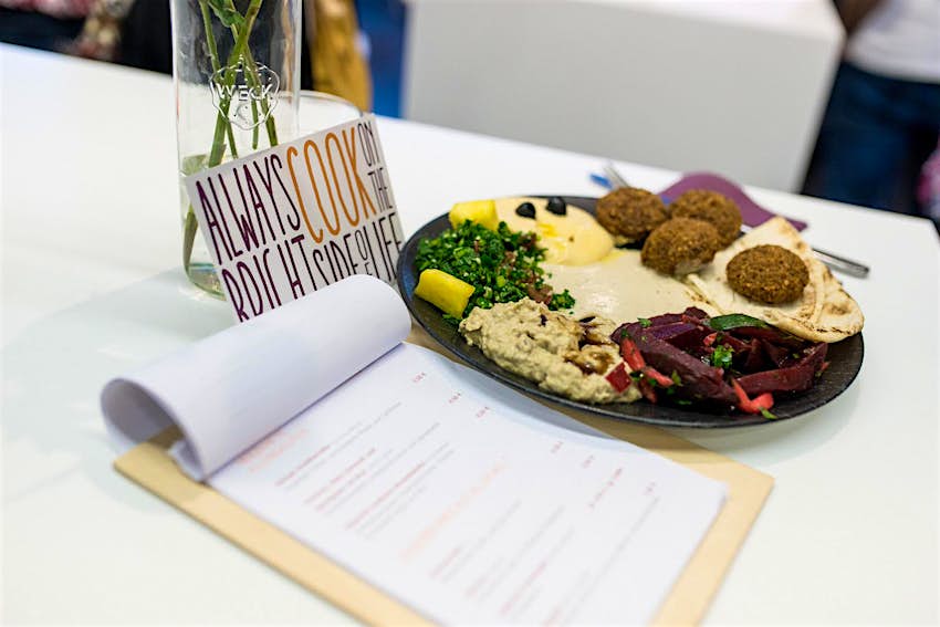 A plate of falafel, hummus and salad next to Über den Tellerrand cafes menu, in Munich. There is also a sign reading 'always cook on the bright side of life' © Über den Tellerrand GmbH