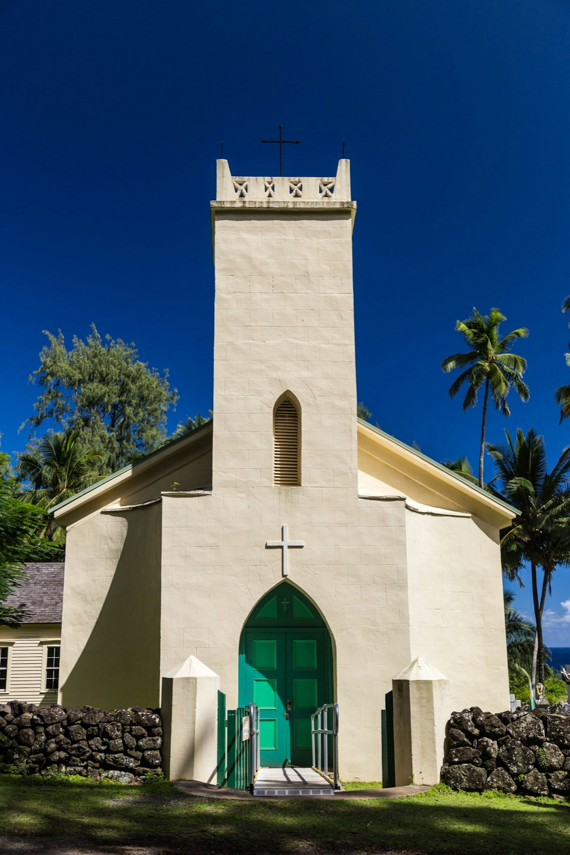 A small, cream-colored church with a bright green arched doorway and a central, rectangular steeple