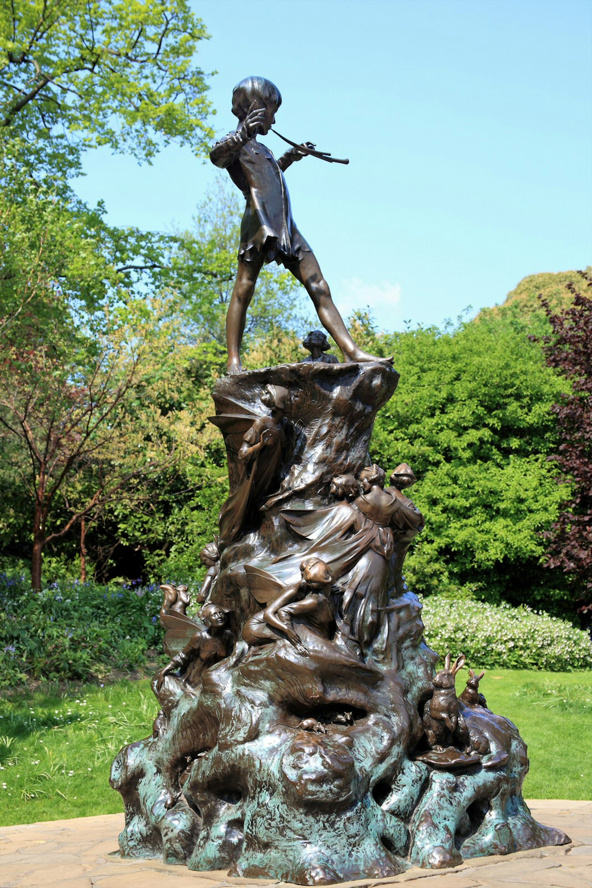 The tall statue of Peter Pan stands amid the greenery of Kensington Gardens in London