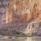 Whitewater rafts and a kayak drift on a calm part of the Colorado River in the Grand Canyon, as sheer rock walls fill the frame behind.