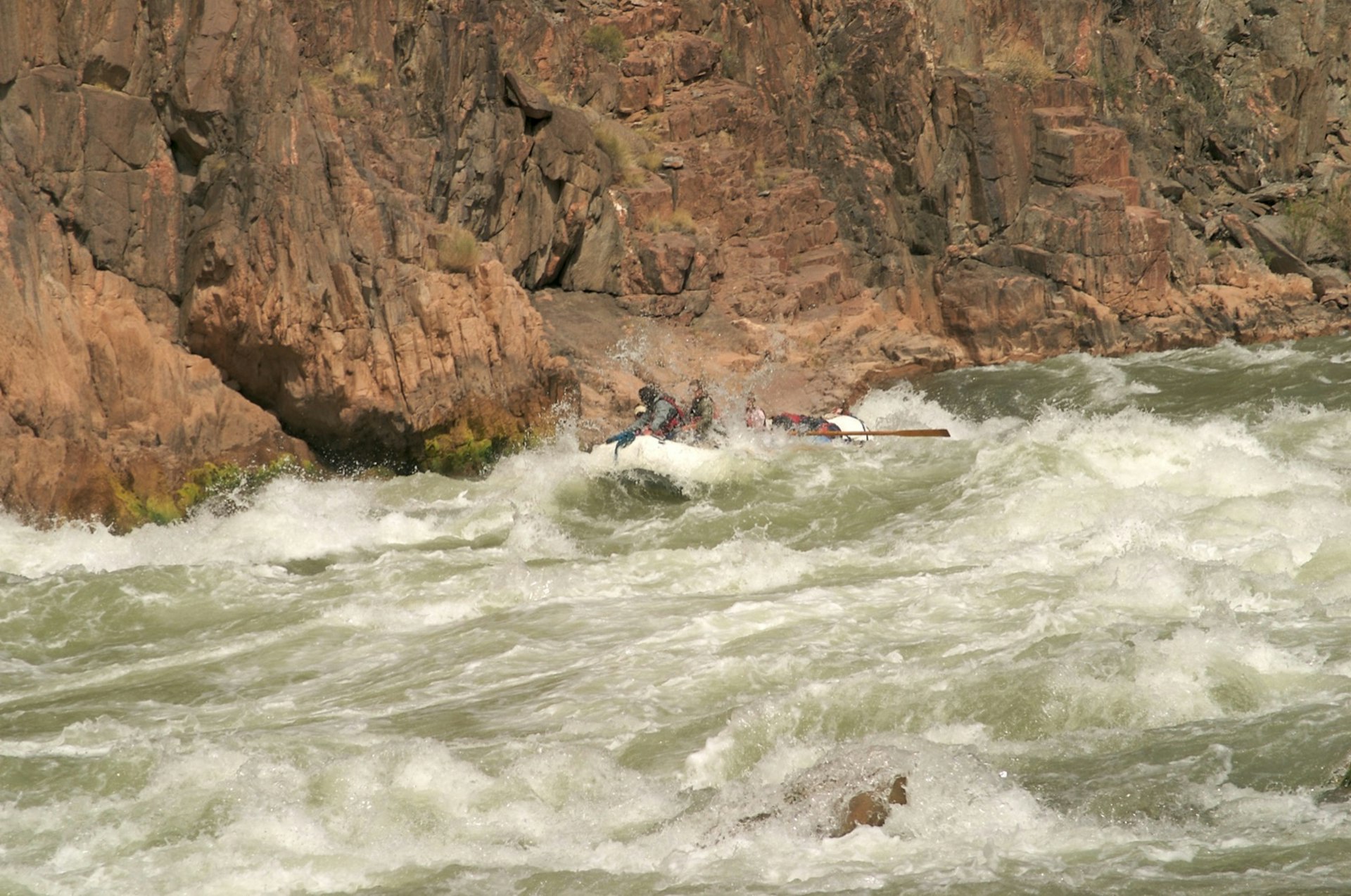 White water engulfs a raft as sheer rock walls rise in the background.