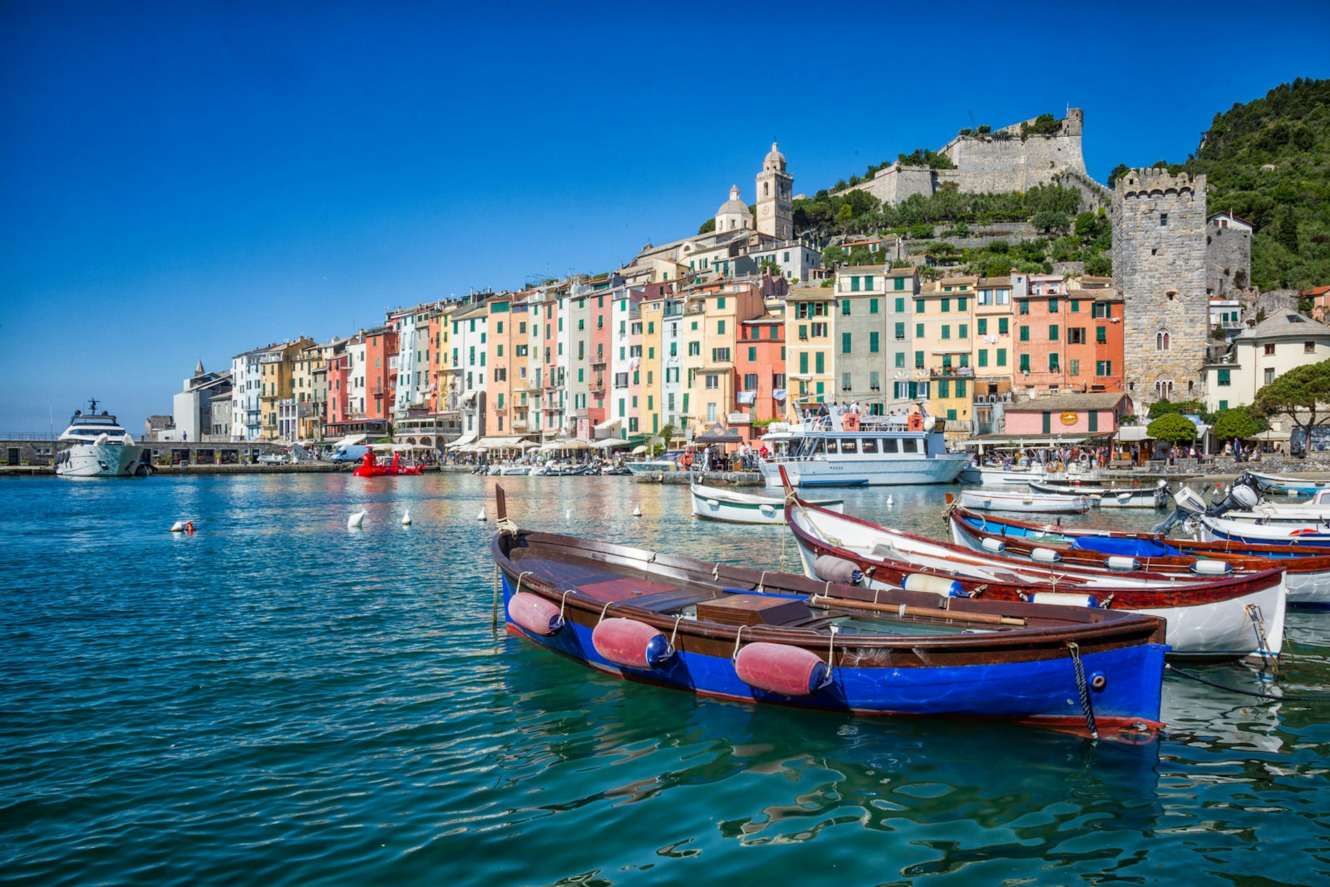 Small boats bob on the sparkling water, whilst the town of Porto Venere rises in the background, topped by a castle