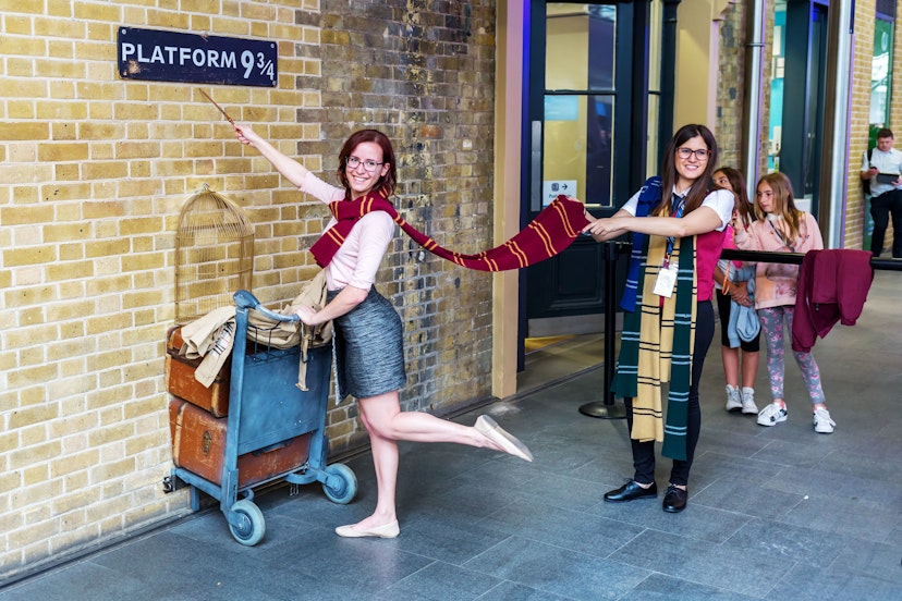 Two people pretend to walk through the wall of Platform 9 at King's Cross Station