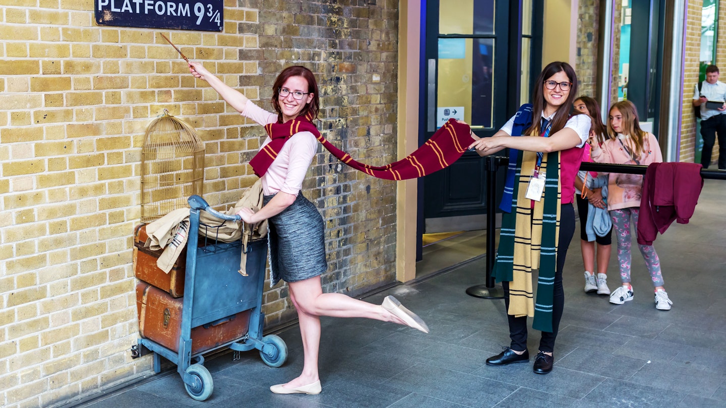 Two people pretend to walk through the wall of Platform 9 at King's Cross Station