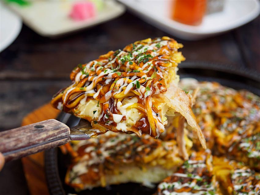 A slice of okonomiyaki is lifted from the plate