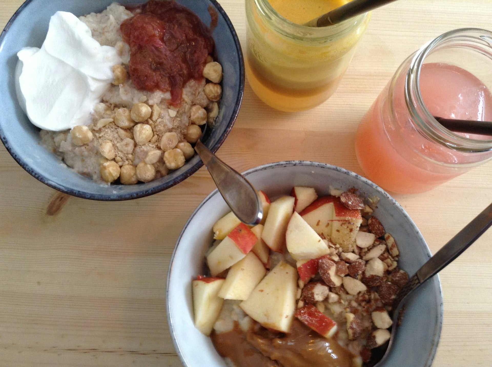 Two bowls of porridge, each covered in different toppings including hazelnuts, yogurt and chopped apple.