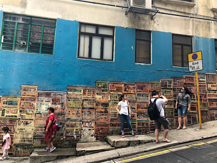A wall painting of tenement houses with people posing for pictures in front of it.