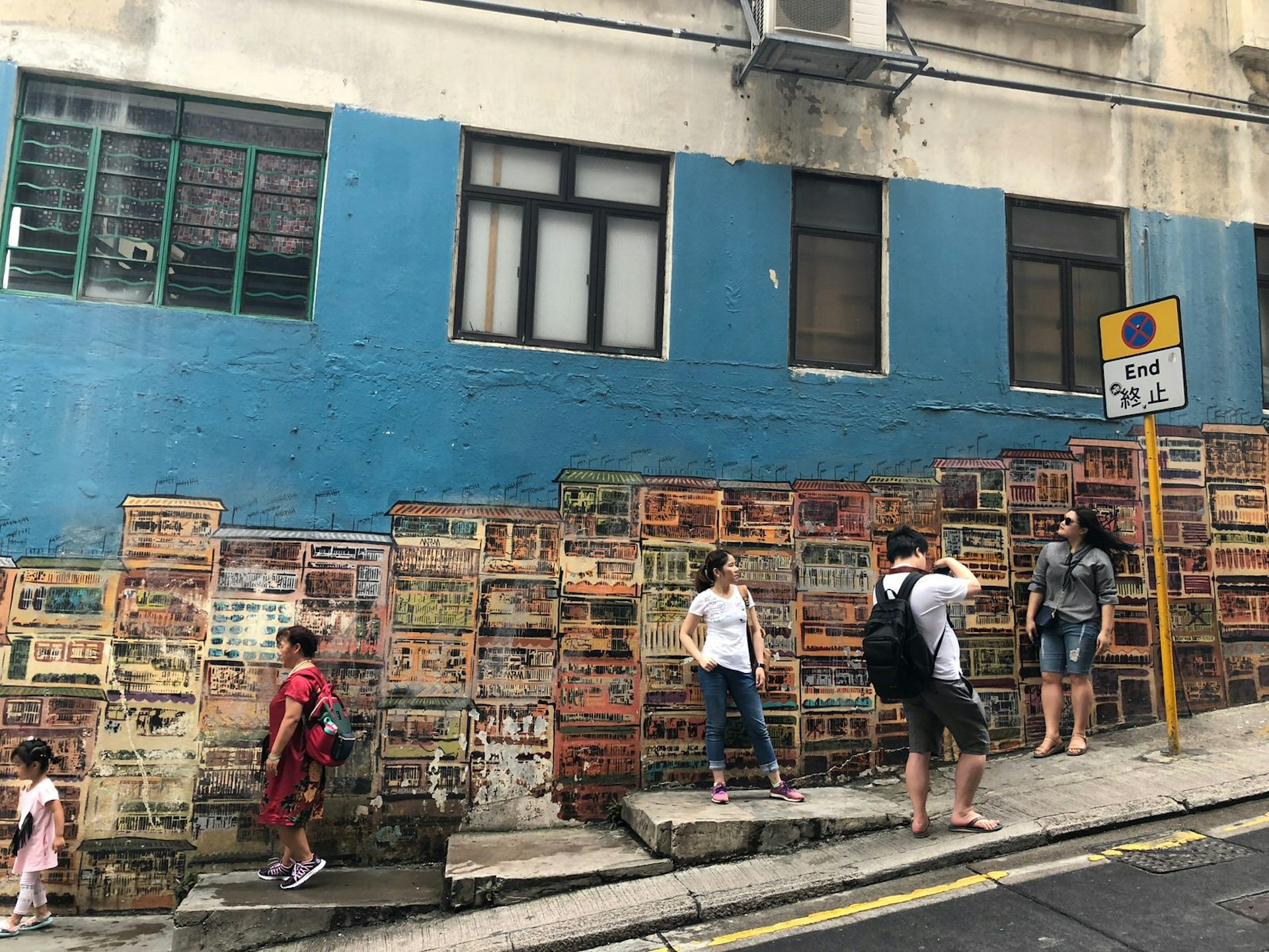 A wall painting of tenement houses with people posing for pictures in front of it.