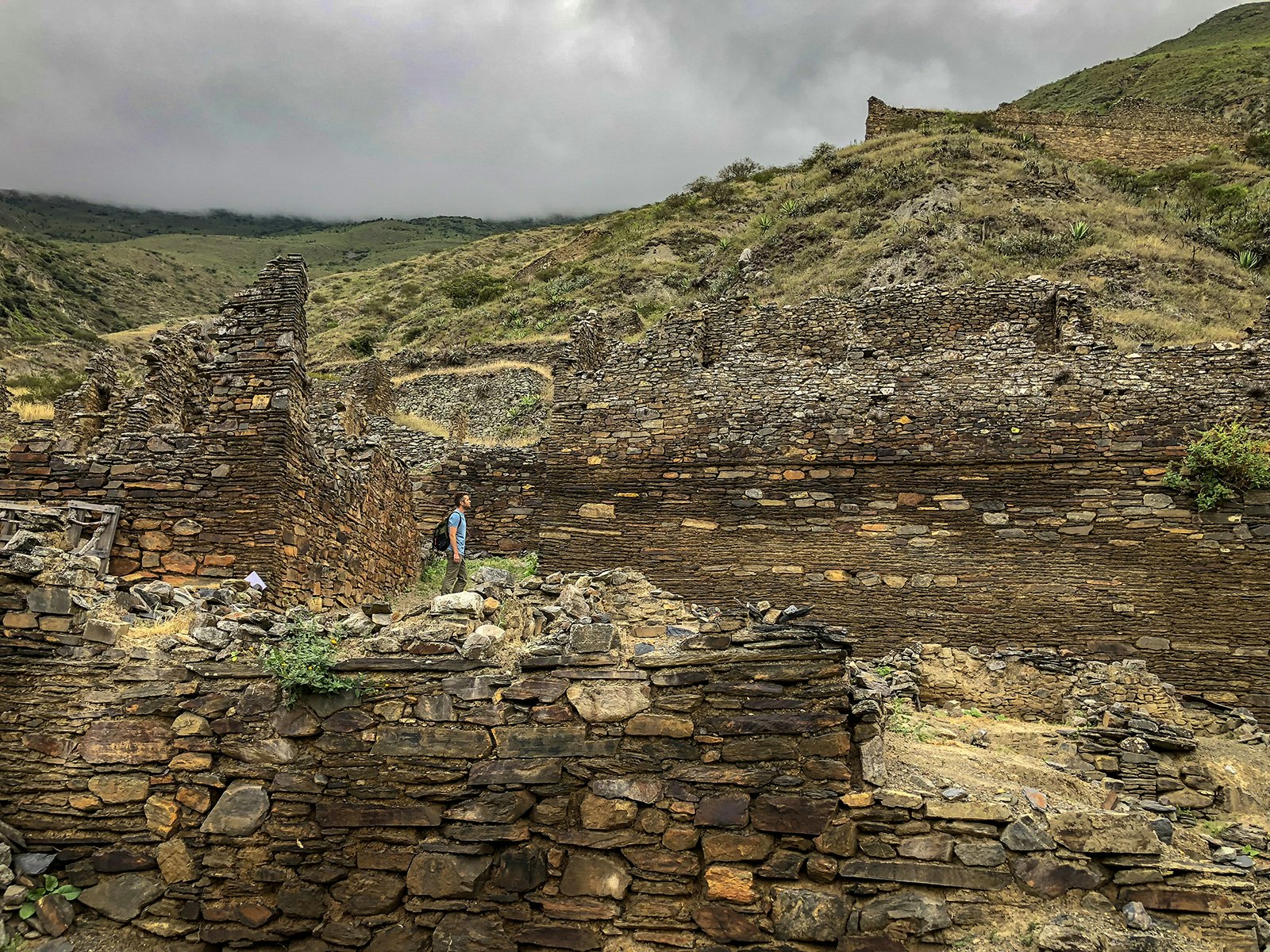 A man stands among ruined stone walls on a cloudy day in Iskanwaya, Bolivia