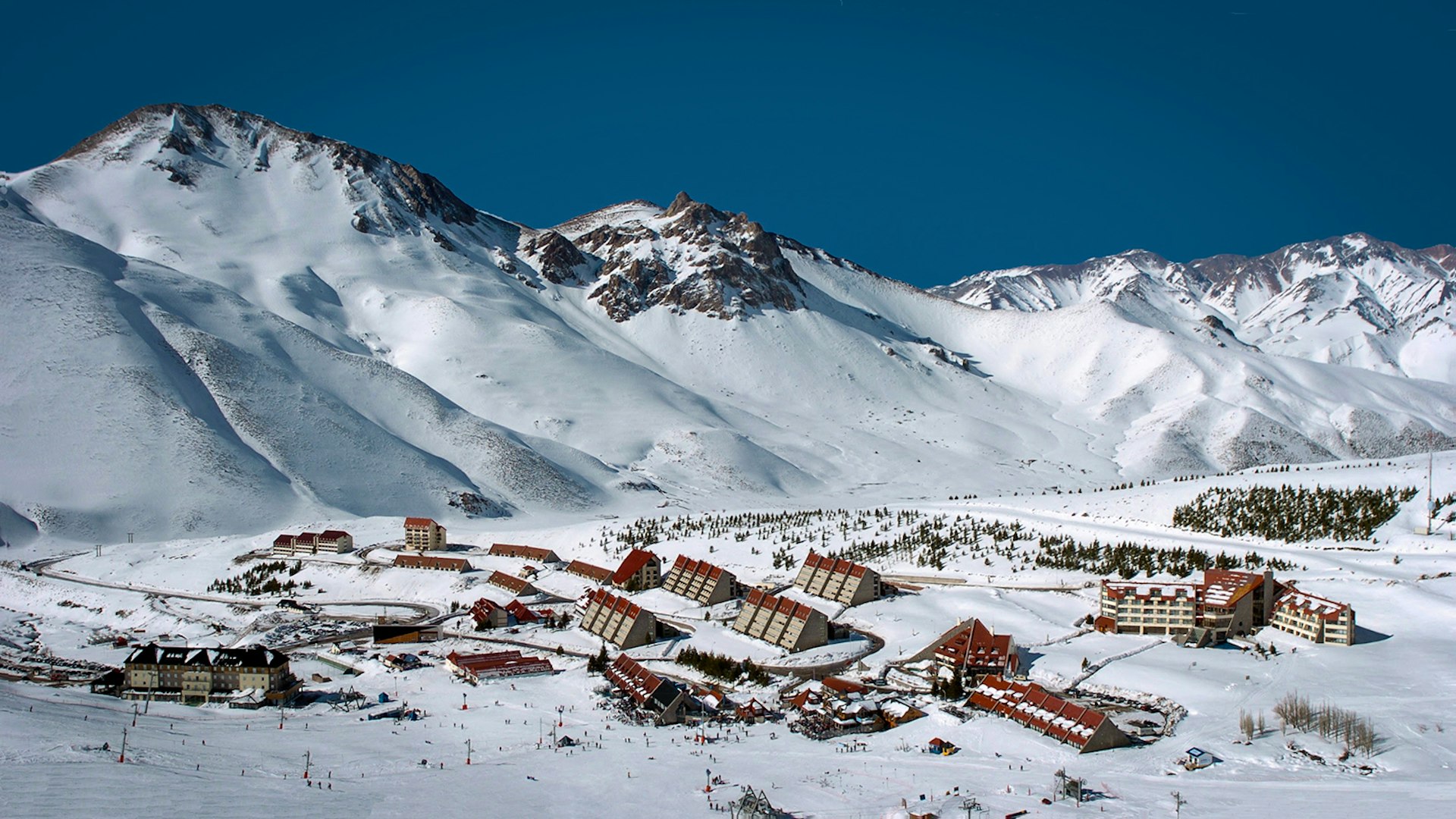 A view of a snow covered mountain range and triangular lodge houses with red roofs at Las Leñas, Argentina