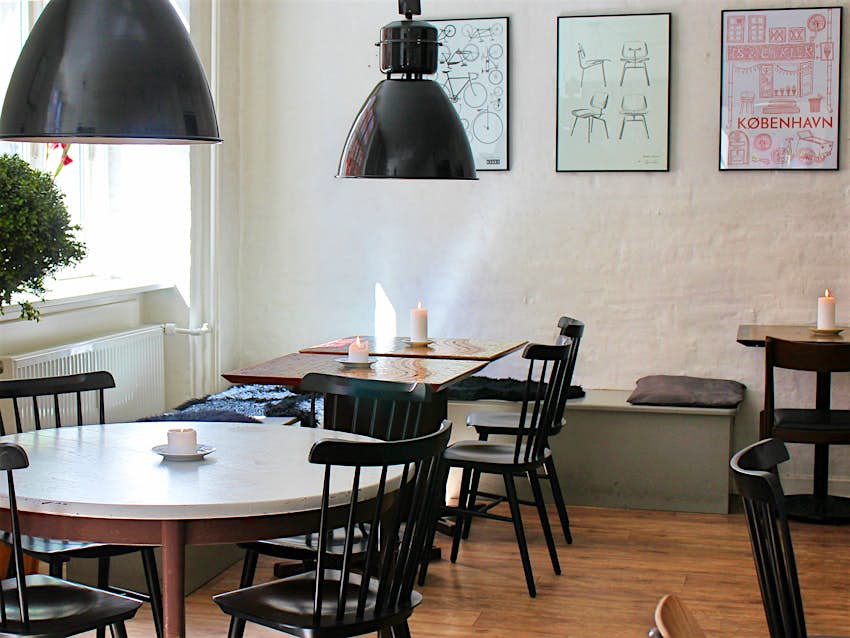 Natural light floods on to matched tables and chairs in the dining room of Mad & Kaffe, Copenhagen. Industrial pendant light fittings hand low from the ceiling and simple but stylish prints adorn the walls.