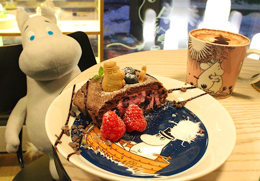 Cake on Moomin-themed crockery at Helsinki's Mumin Kaffe, with a Moomin stuffed toy at the table