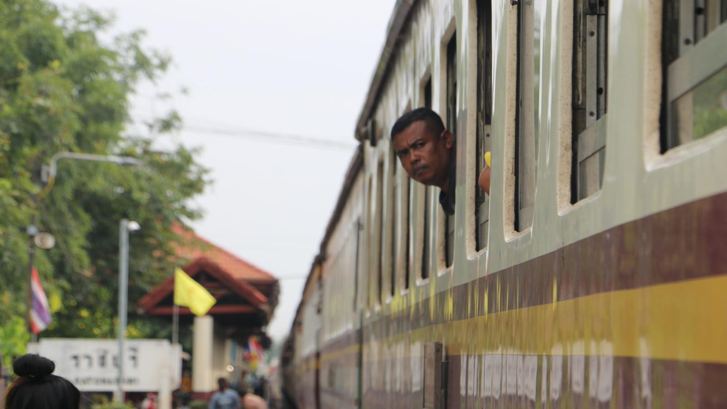A man peeps his head out of a train window en route to Bangkok