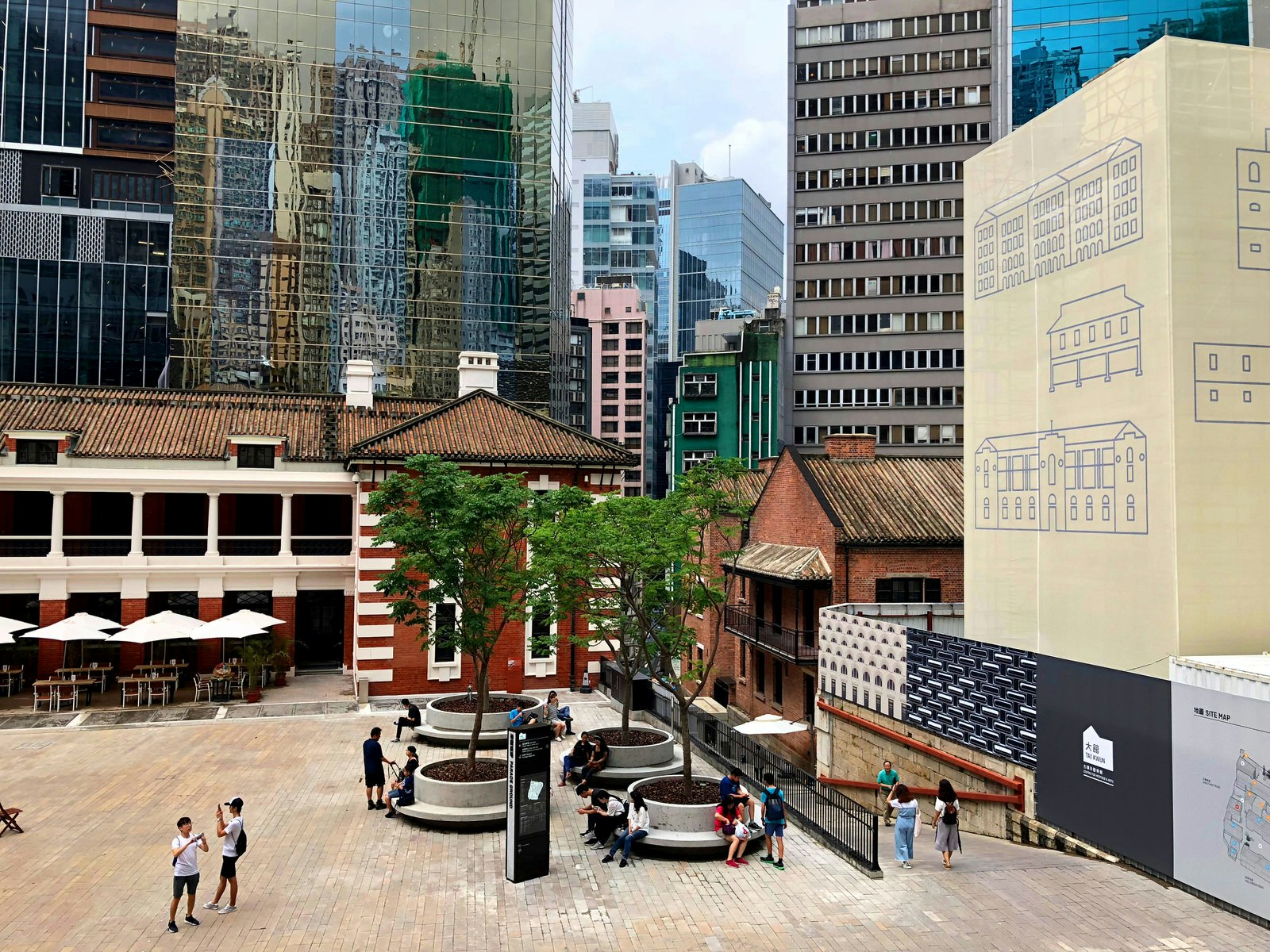 An overview of the inner courtyard of Tai Kwun, with brick buildings surrounded by tall glass skyscrapers
