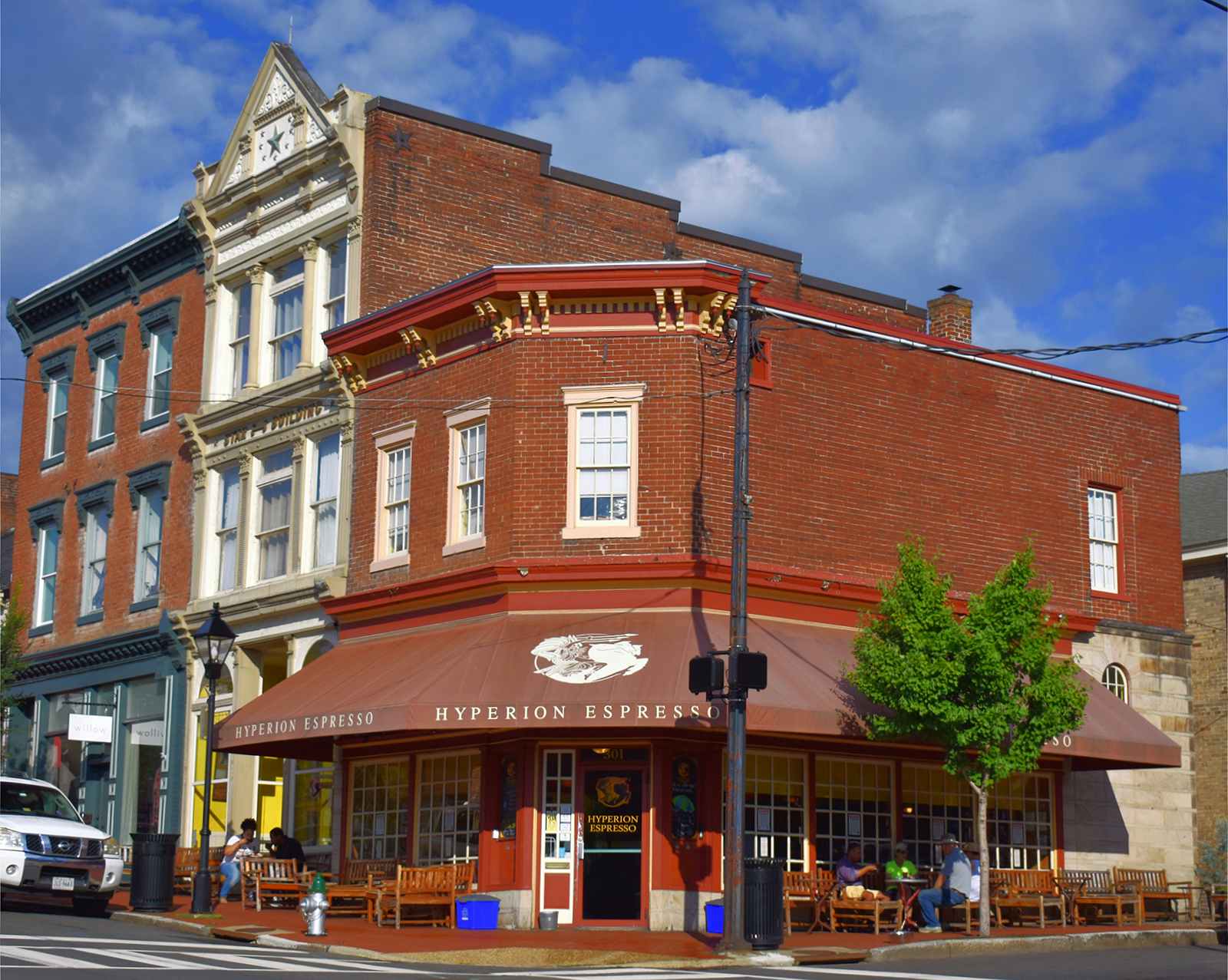 A corner shop in red brick with a maroon awning bearing the words "Hyperion Espresso" on a sunny day in Virginia