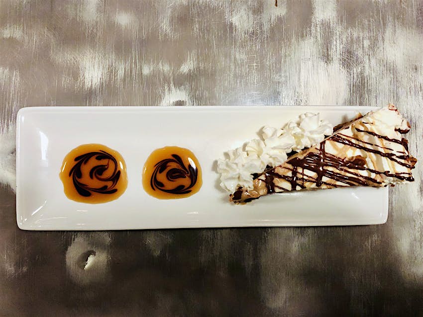 aerial shot of a slice of peanut-butter pie topped with whipped cream and drizzles of butterscotch and chocolate syrup on a white plate with puddles of caramel sauce