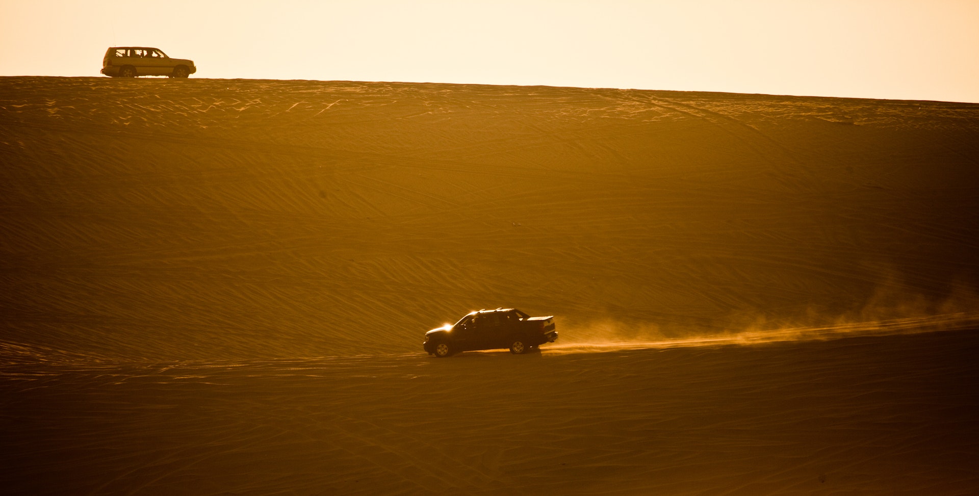 Two trucks drive off road in the sandy desert in Qatar
