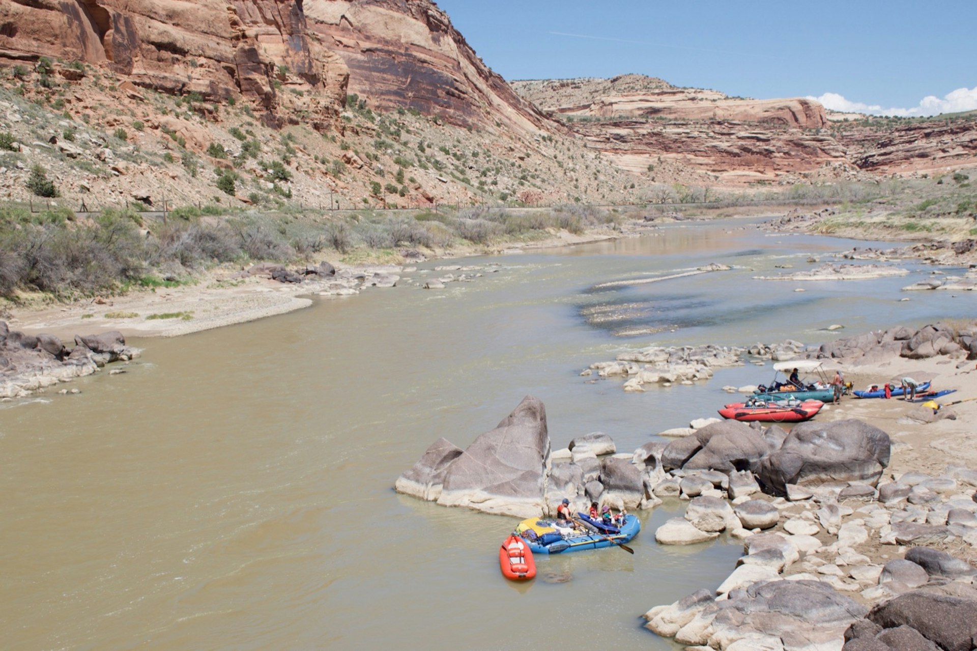 Several rafts are arranged along the banks of a fairly calm river in the southwest, with dusty hills rising beyond.