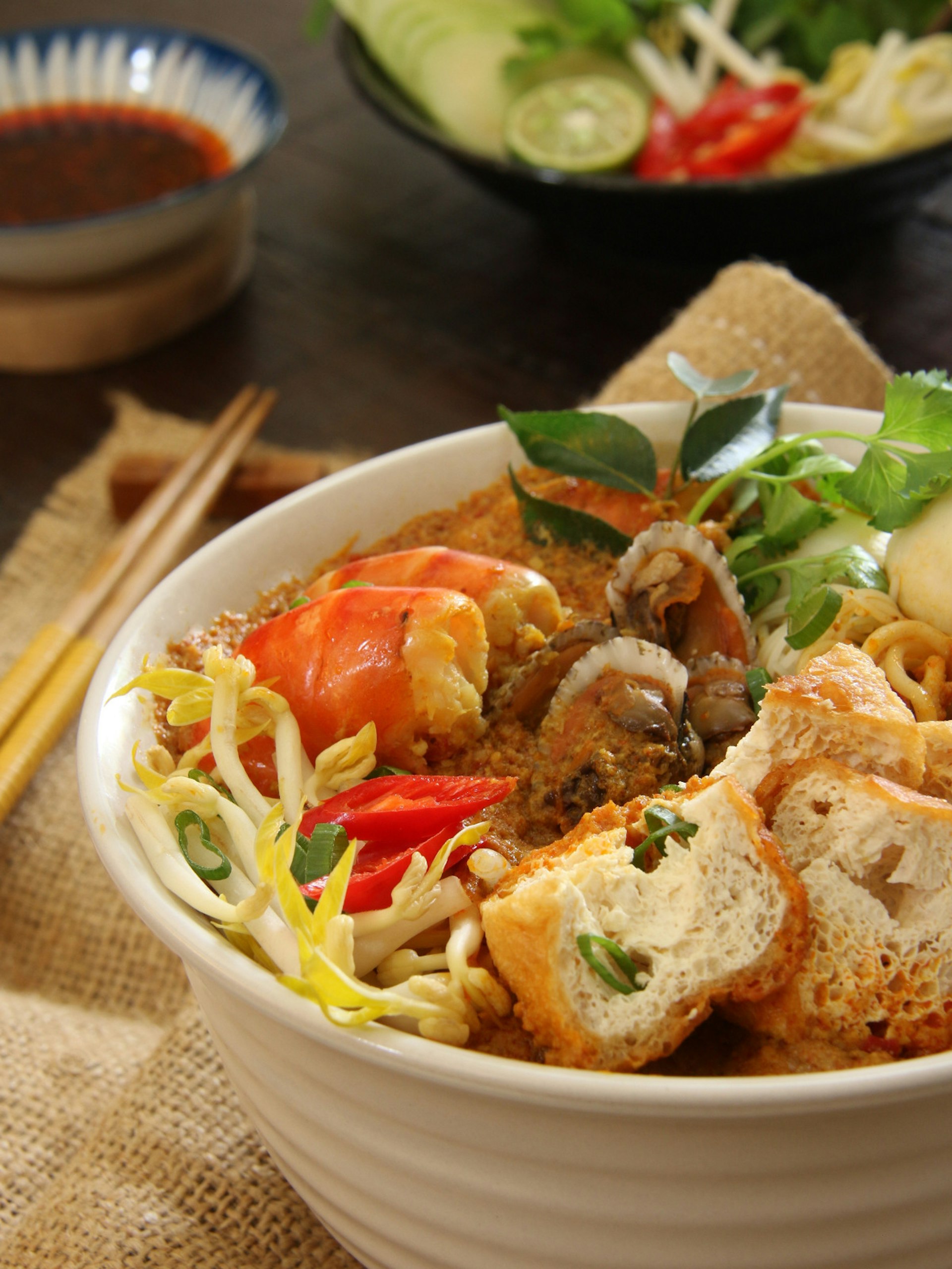Peranakan laksa served in a bowl, accompanied with chili sauce and extra vegetables
