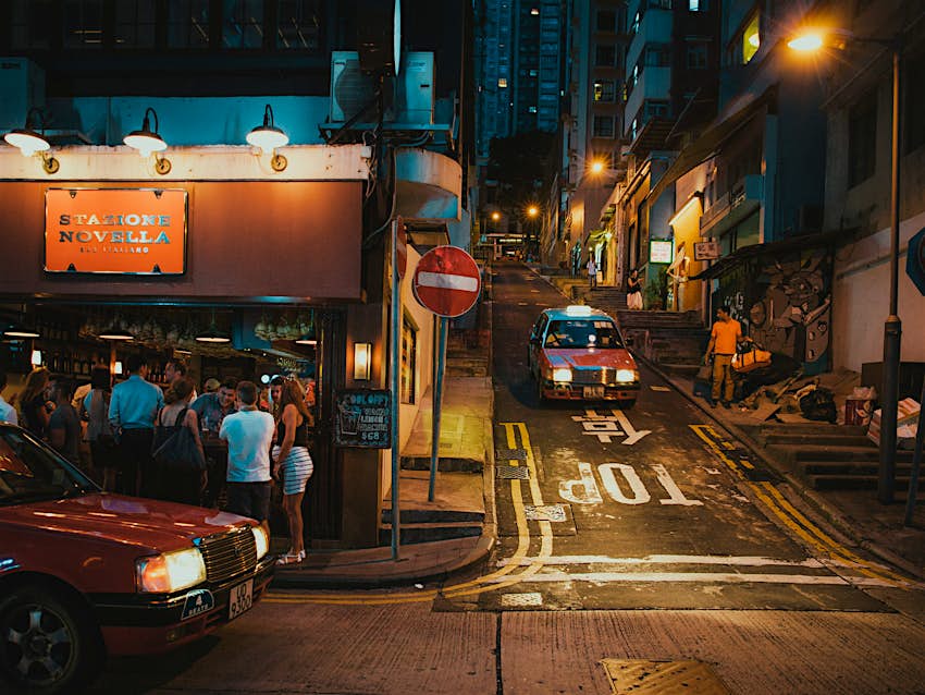 Two Hong Kong red taxis meet at a junction of narrow streets lit by evening street lights