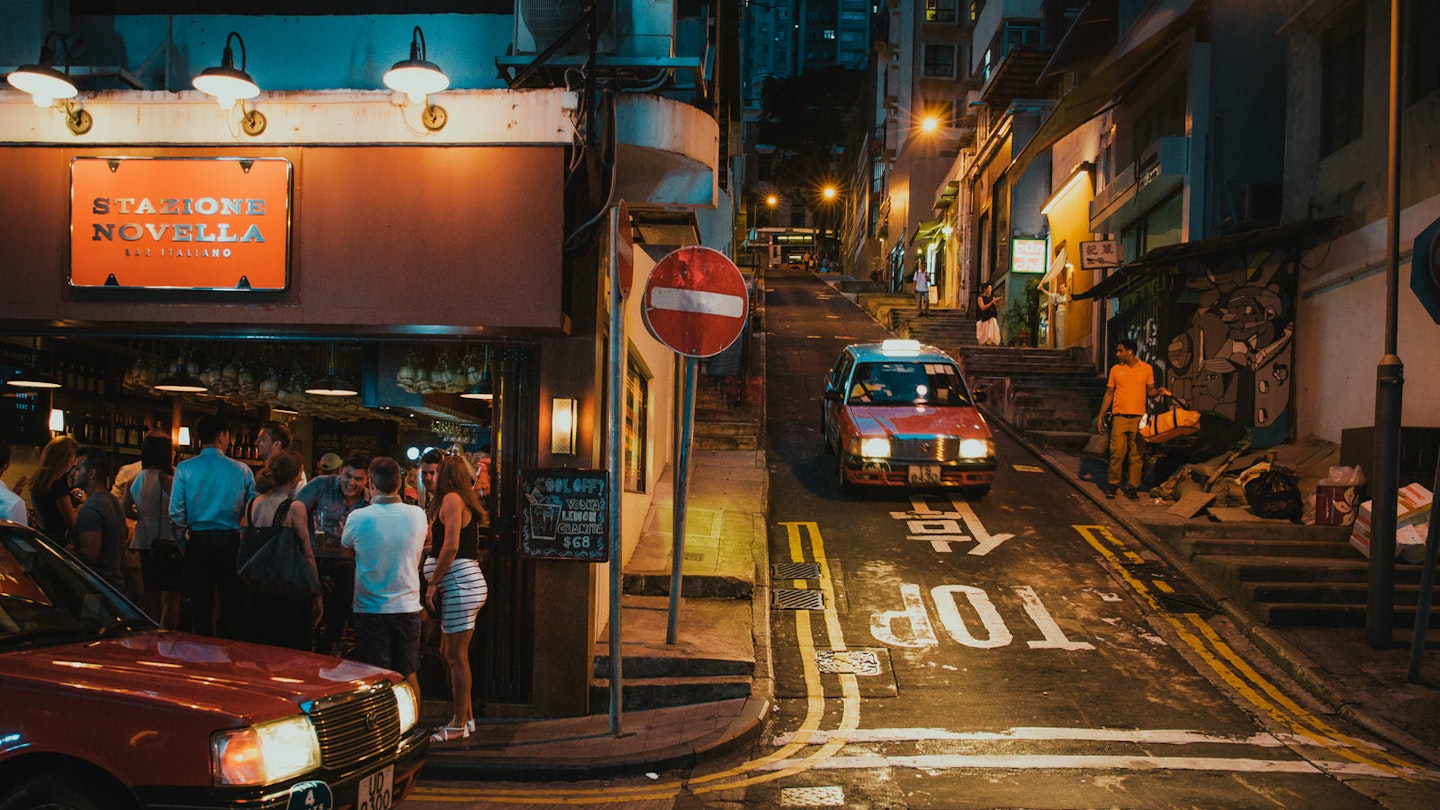 Two Hong Kong red taxis meet at a junction of narrow streets lit by evening street lights