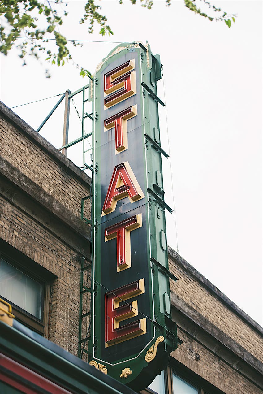 Green vertical sign with the word "State" in red letters, on the brick facade of the State Theater in Ithaca New York