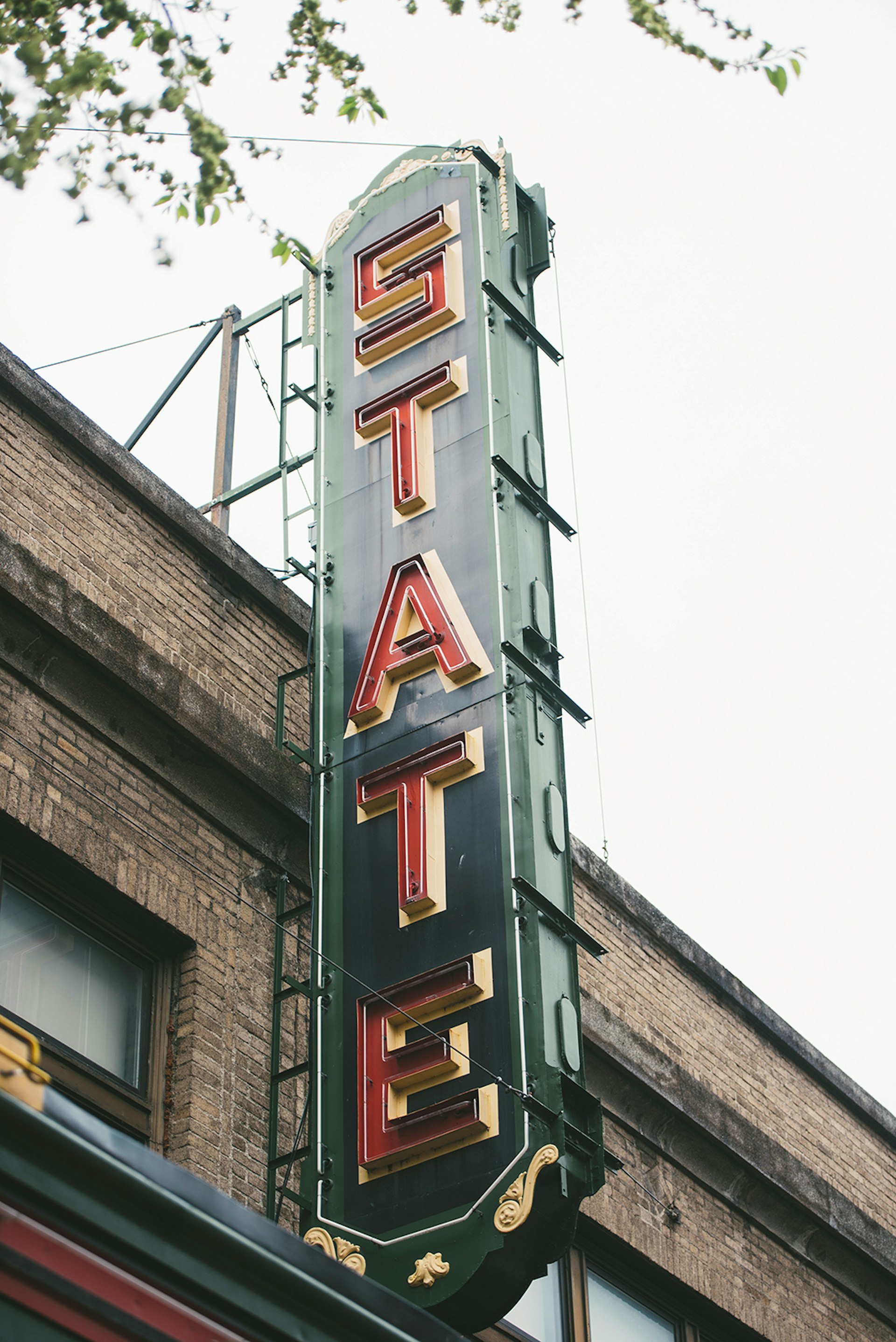 Green vertical sign with the word "State" in red letters, on the brick facade of the State Theater in Ithaca New York