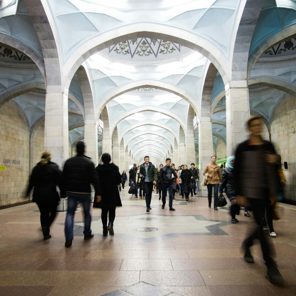 View of Alisher Navoi station with its blue arched domes and blurred passengers walking down the platform.