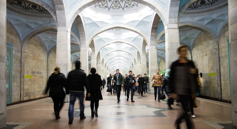 View of Alisher Navoi station with its blue arched domes and blurred passengers walking down the platform.