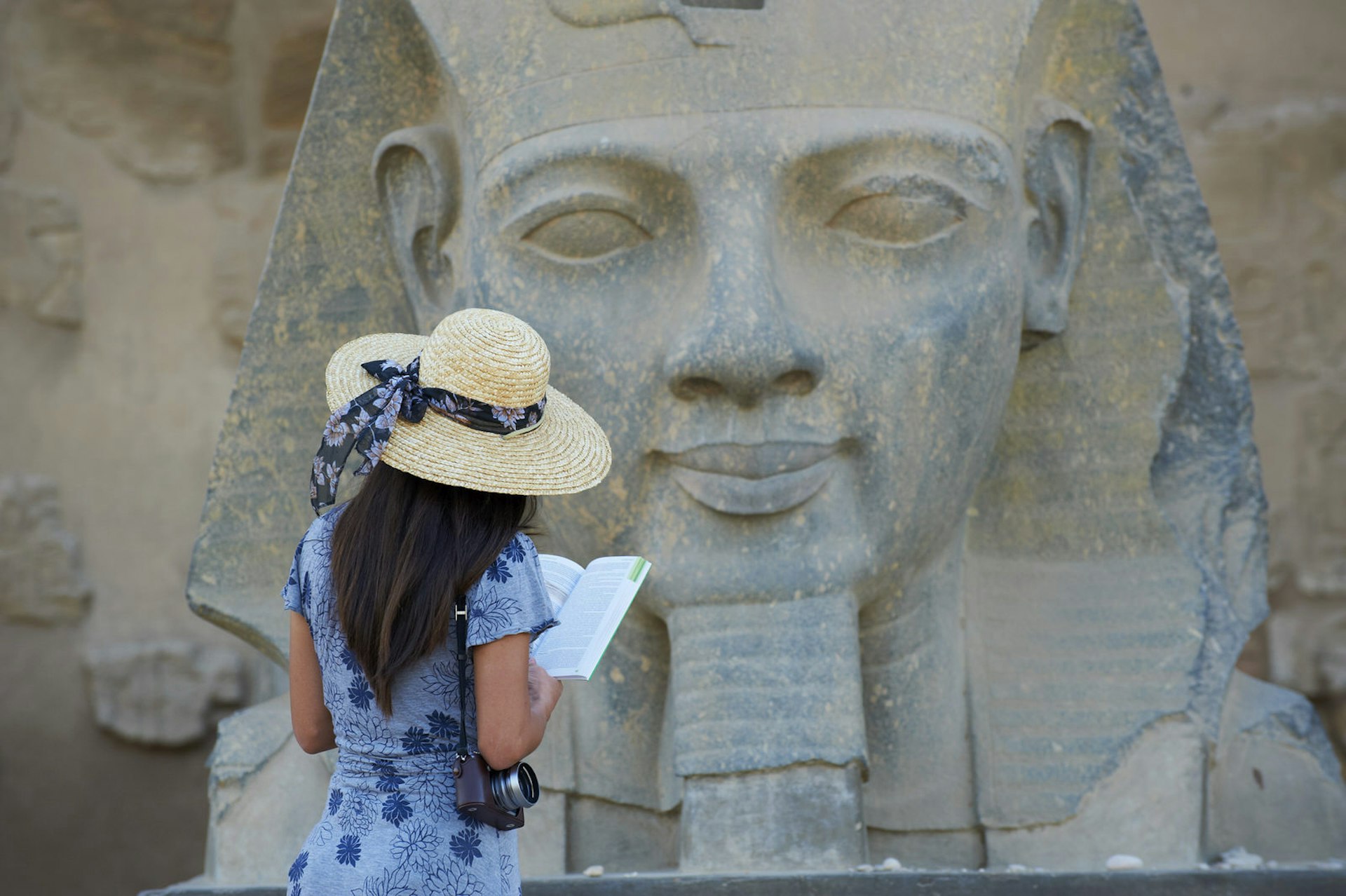 Tourist reads a guidebook and studies a statue of the pharaoh Ramses II, Temple of Luxor, Egypt