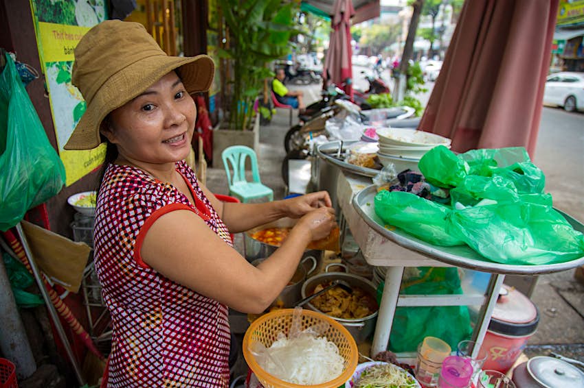 A woman making mi quang noodles smiles at the camera