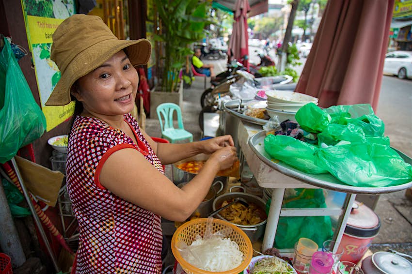 Features - Trang sells Mi Quang on the street A woman making mi quang noodles smiles at the camera