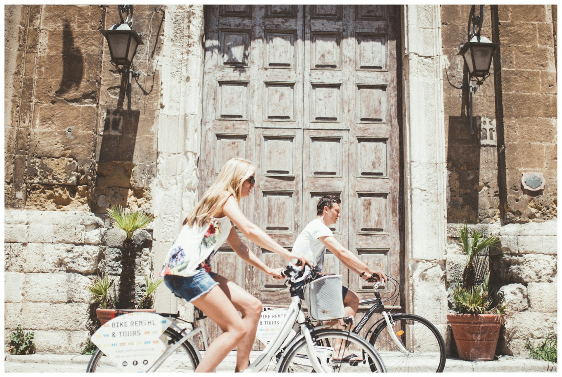 Two cyclists ride past a large wooden doorway