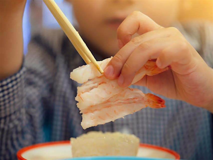 Young boy eating sushi with chopsticks