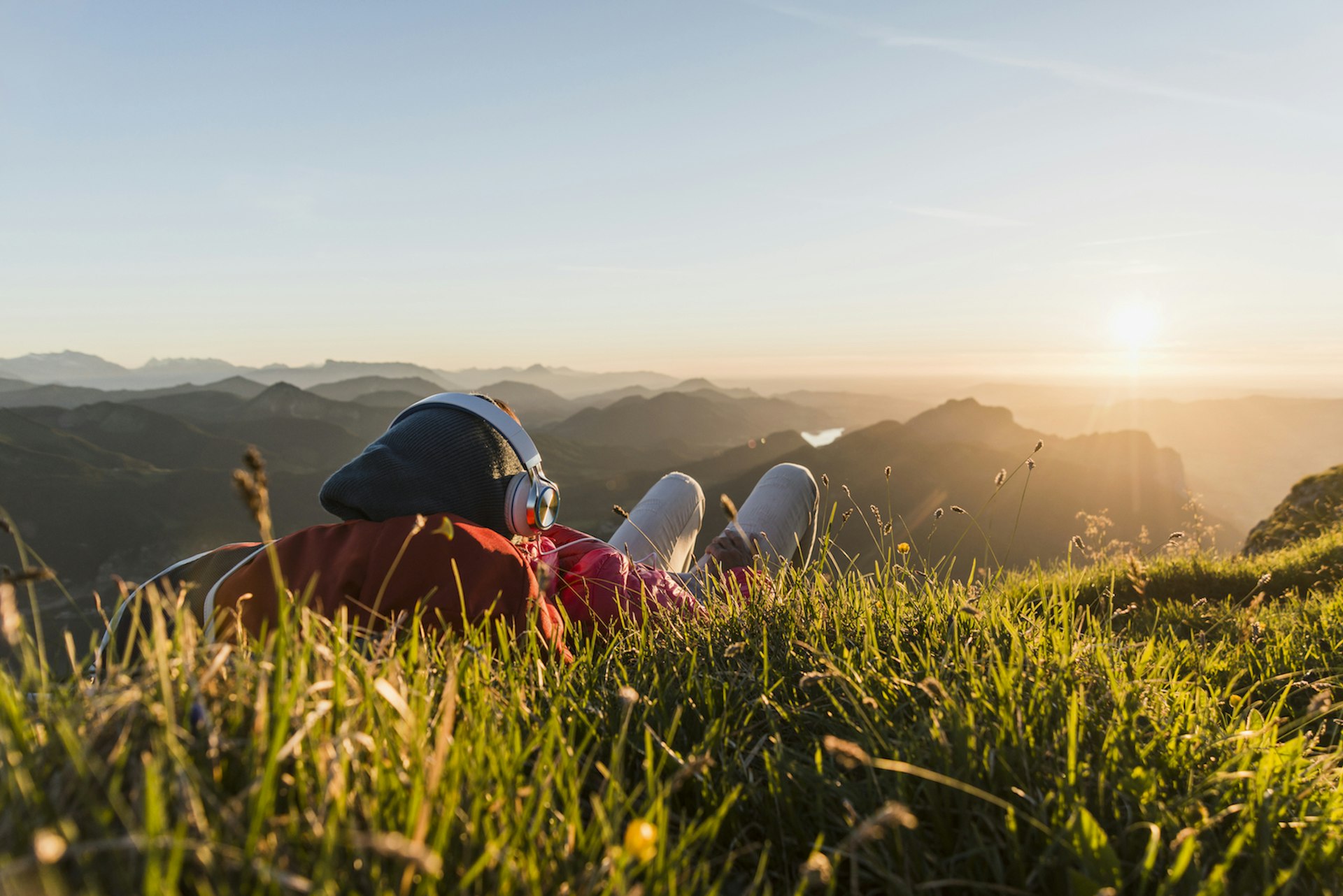 Hiker lying in grass, taking a break and listening music with headphones