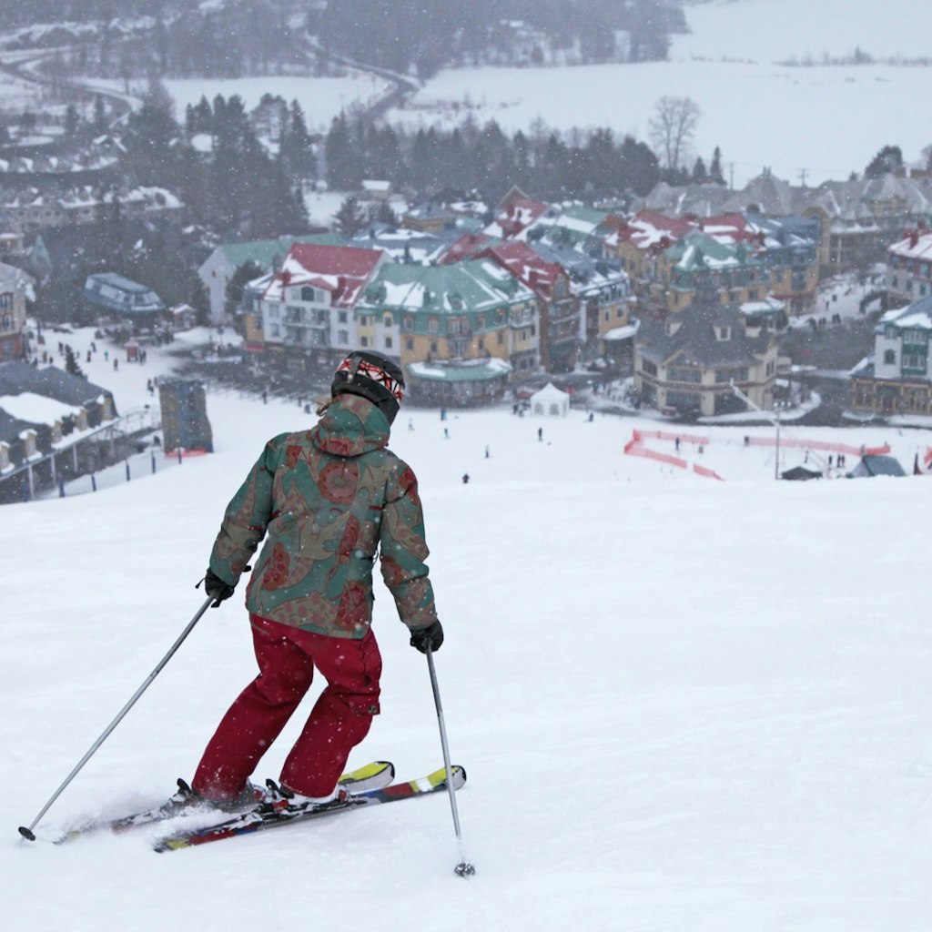 A woman skis on top of a mountain as a picturesque village, covered in snow, spreads out below her at the foot of the slope