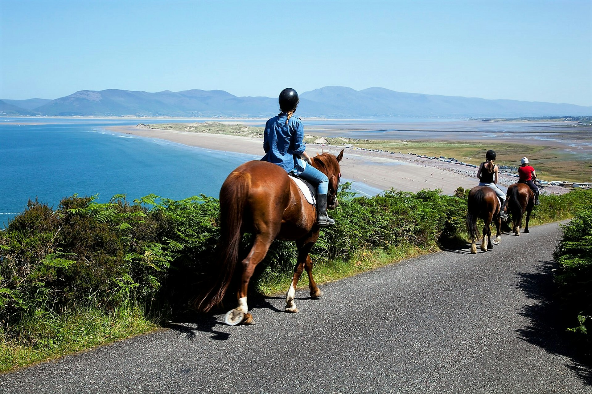 Horse and rider in narrow road with view of a sandy beach and some hills