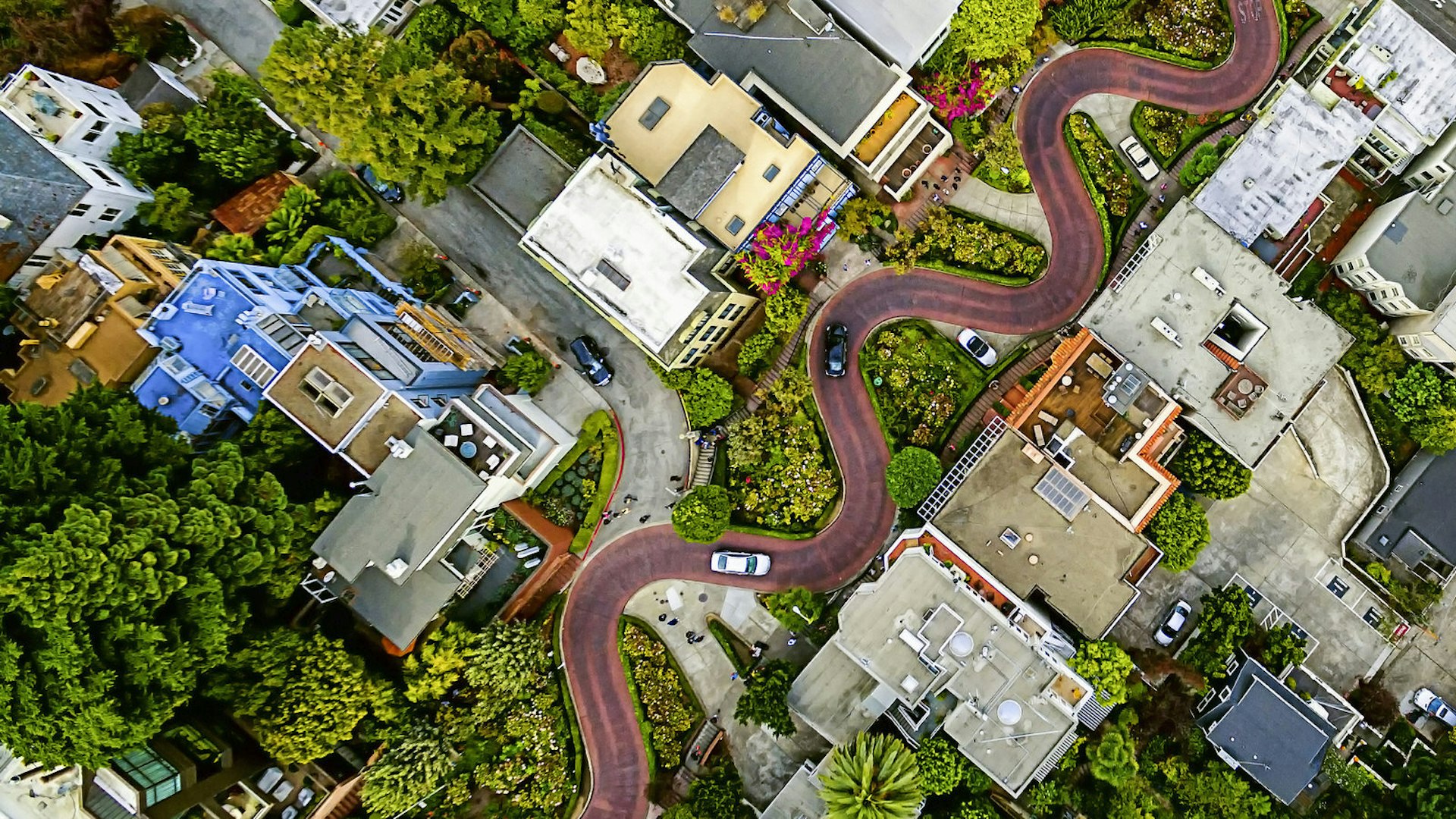 Aerial view of a residential city area, with road descending a hillside with eight hairpin turns.